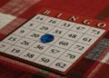 Bingo card on a red plaid tablecloth, with numbers and a blue chip on square "B 12." The setting feels cozy and inviting, suggesting a game in progress.
