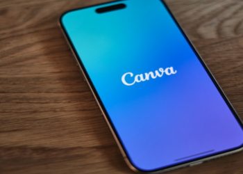 Smartphone on a wooden table displaying the Canva app with a blue to purple gradient background, conveying a modern, creative vibe.