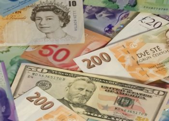 Assortment of international banknotes, including British pounds, Canadian dollars, Czech korunas, and U.S. dollars, spread out randomly.