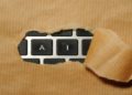 Piece of brown paper ripped open reveals a keyboard underneath, with the visible keys spelling "AI". The image suggests discovery or unveiling of technology.