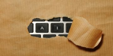 Piece of brown paper ripped open reveals a keyboard underneath, with the visible keys spelling "AI". The image suggests discovery or unveiling of technology.