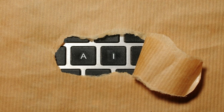 Piece of brown paper ripped open reveals a keyboard underneath, with the visible keys spelling "AI". The image suggests discovery or unveiling of technology.