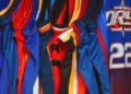 Row of colorful basketball jerseys hang closely together, featuring various designs and team colors. The scene conveys a sense of sport and team spirit.