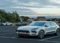 Silver car is parked in an almost empty lot under a cloudy sky at dusk, with a brick building and trees in the background, creating a serene scene.