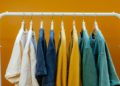 White clothing rack displays colorful T-shirts in shades of white, blue, yellow, and green against a vibrant orange background, creating a cheerful and stylish scene.