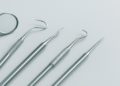 Five stainless steel dental tools, including a mirror and probes, are neatly arranged on a light gray background, conveying a clean, clinical atmosphere.