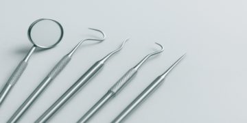 Five stainless steel dental tools, including a mirror and probes, are neatly arranged on a light gray background, conveying a clean, clinical atmosphere.