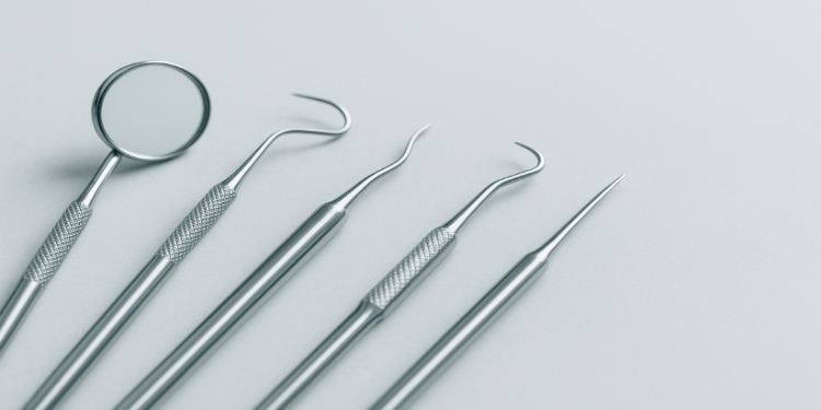 Five stainless steel dental tools, including a mirror and probes, are neatly arranged on a light gray background, conveying a clean, clinical atmosphere.
