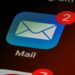 Close-up of a smartphone screen showing apps with a focus on the Mail app icon. The app displays a red notification badge with the number two, indicating new messages.