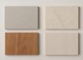 Four rectangular material samples are arranged in a grid on a light surface. Top left: gray speckled; top right: beige marble; bottom left: reddish wood; bottom right: light wood.