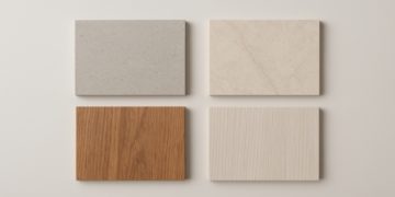 Four rectangular material samples are arranged in a grid on a light surface. Top left: gray speckled; top right: beige marble; bottom left: reddish wood; bottom right: light wood.