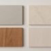 Four rectangular material samples are arranged in a grid on a light surface. Top left: gray speckled; top right: beige marble; bottom left: reddish wood; bottom right: light wood.