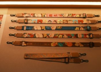 Display of seven colorful lanyards with cartoon designs and clips, laid horizontally on a lit surface. The mood is playful and vibrant.