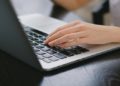 Hand typing on a laptop placed on a dark wooden table. The image conveys productivity and focus, with a close-up view of the keyboard.