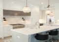Modern kitchen with white cabinetry, a central island, black chairs, and pendant lights. The space exudes elegance and brightness, with marble accents.