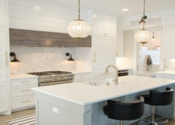 Modern kitchen with white cabinetry, a central island, black chairs, and pendant lights. The space exudes elegance and brightness, with marble accents.