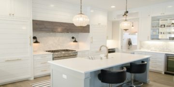 Modern kitchen with white cabinetry, a central island, black chairs, and pendant lights. The space exudes elegance and brightness, with marble accents.