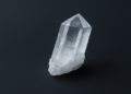 Clear quartz crystal with sharp, faceted edges stands upright against a dark background, conveying a sense of clarity and serenity.