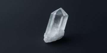 Clear quartz crystal with sharp, faceted edges stands upright against a dark background, conveying a sense of clarity and serenity.