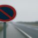 No parking sign stands beside an empty, foggy road. The muted tones convey a sense of isolation and calm on the misty, deserted highway.
