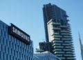 Modern cityscape with a Samsung building in the foreground, a tall residential tower, and additional skyscrapers against a clear blue sky.