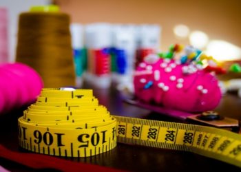 Vibrant sewing scene with a yellow measuring tape, colorful spools of thread, a pincushion filled with pins, and scissors. The atmosphere is creative and lively.