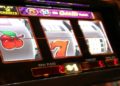 Slot machine close-up showing three reels with a cherry, the number seven, and blank spaces. Display shows win paid as 2, with light glow.