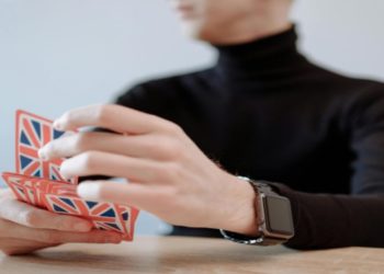 Person in a black turtleneck shuffles playing cards decorated with Union Jack flags. The focus is on their hands, creating a thoughtful and calm atmosphere.
