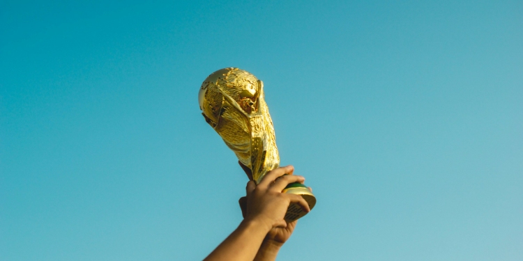 Hands raise a golden trophy against a clear blue sky, symbolizing triumph and celebration. The moment is uplifting and victorious.