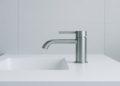 Sleek modern bathroom with a minimalist design. A metallic faucet extends over a white countertop with an inset sink, set against light gray tiled walls.