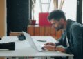 Photographer editing images on a laptop at a desk with cameras beside him