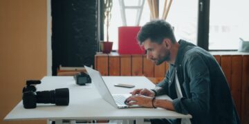 Photographer editing images on a laptop at a desk with cameras beside him