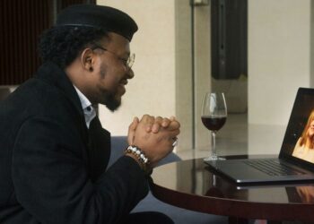 Man smiling on a video call date with a woman on his laptop, glass of red wine on the table