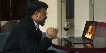 Man smiling on a video call date with a woman on his laptop, glass of red wine on the table