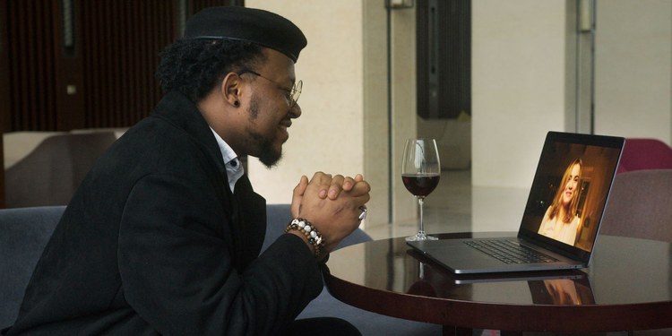 Man smiling on a video call date with a woman on his laptop, glass of red wine on the table